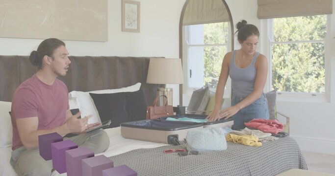 Packing couple arranging clothes on bed in bedroom with open suitcase and scattered travel items