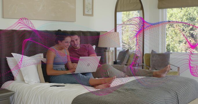 Browsing couple sitting on king bed in bedroom, viewing laptop with magenta wave wearing shorts
