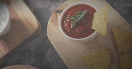 Displaying white bowl holding tomato salsa with rosemary on wooden board in kitchen, tortilla chips © vectorfusionart