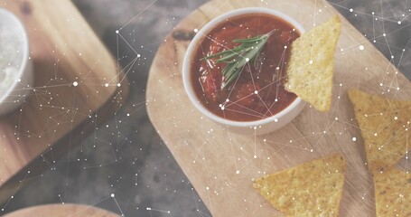 Featuring white bowl of red salsa with rosemary on wooden board, chips and constellation overlay © vectorfusionart