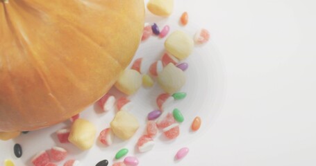 Displaying partial orange pumpkin resting on smooth white tabletop, with bright candies, copy space © vectorfusionart