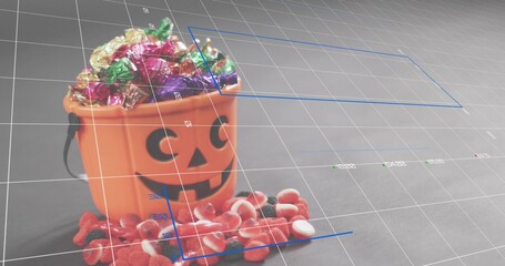 Displaying orange jack-o'-lantern bucket holding foil candies on gray tabletop with blue guides © vectorfusionart
