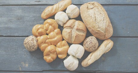 Showing breads resting on weathered blue-gray plank, featuring crusty loaf, baguettes, seeded rolls