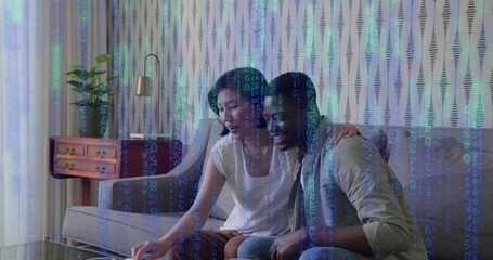 Leaning couple wearing white blouse and shirt reaching tablet on glass coffee table, code overlay