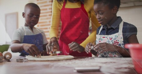 Baking mom and two kids wearing aprons pressing metal cookie cutters into dough at home kitchen