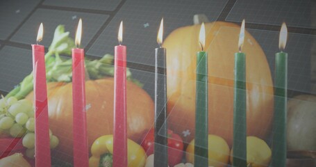 Flickering row of red black green tapered candles glowing on kitchen table with pumpkin, grapes