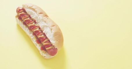 Sitting hot dog in soft bun on studio tabletop with mustard and ketchup drizzle, copy space