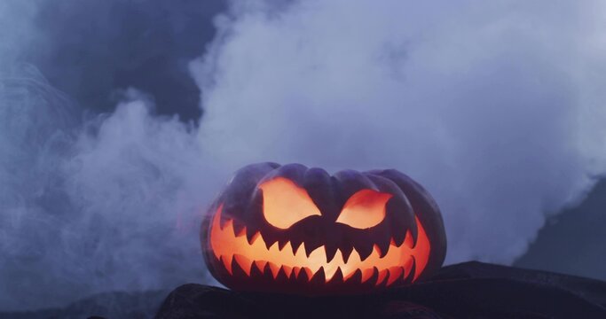 Glowing carved jack-o'-lantern casting warm orange light on dark rocky surface, with fog