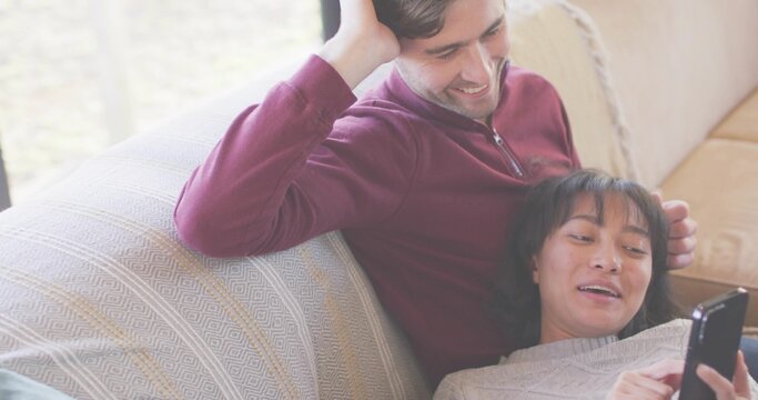 Sitting couple on living room patterned couch, woman using phone leaning into man in maroon sweater - Powered by Adobe