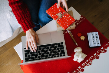 Obraz premium Person writes CHRISTMAS SHOPPING LIST in notebook while holding small gift box on white coffee table. Online shopping, seasonal ecommerce, Christmas sales, holiday planning.