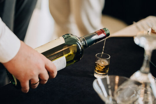 Hand pouring alcohol from bottle into shot glass