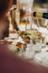 Hand pouring white wine into glass at dinner