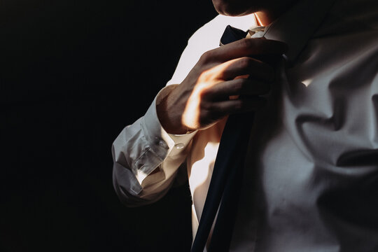 Man adjusting tie by hand in dramatic light