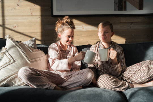 siblings drinking hot chocolate together on a sofa in pyjamas at home
