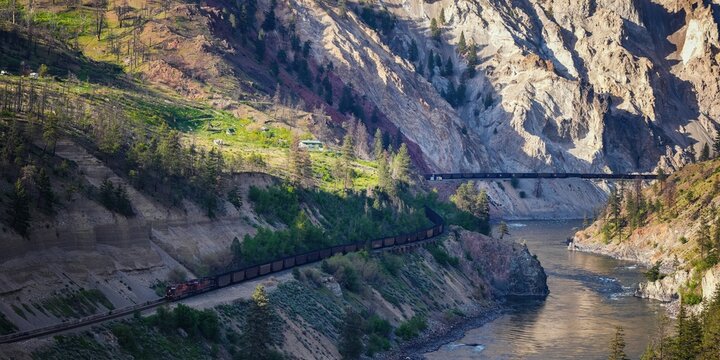 Long cargo train moving along the mountainside with a river flow