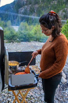 Woman cooking pasta bolognese outside camper van in the mountains