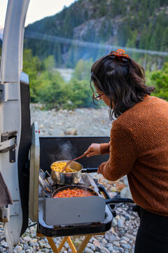 Woman cooking pasta bolognese outside camper van in the mountains