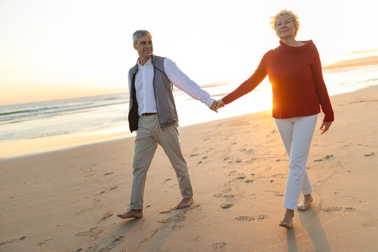 Senior couple holding hands walking beach at sunset