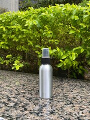 Silver Spray Bottle on Outdoor Stone Surface with Green Background