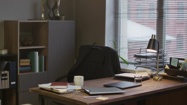 Handheld shot of modern principals office with clipboards on shelves, and desk with laptop and documents in school