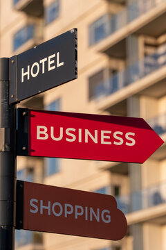 A clear and eye-catching signpost providing essential navigation directions for travelers, featuring categories like hotel, business, and shopping in a vibrant urban setting.