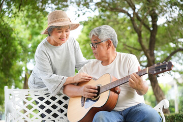 Senior couple enjoying music together outdoors with man playing acoustic guitar, Happy elderly couple relaxing in park while playing and listening to guitar