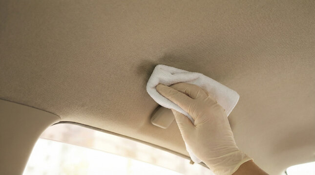 Cleaning beige car roof lining or headliner with white microfiber cloth and cleaner