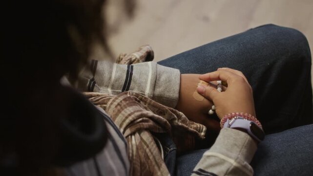 High angle view of stressed teenage girl fidgeting with bandage on hand while sitting anxiously in school office