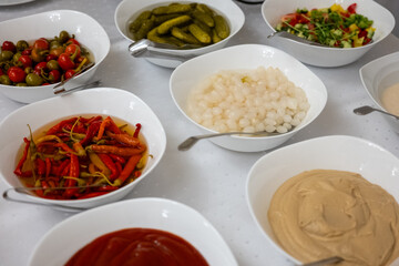 Various pickled vegetables, sauces, and dips served in white bowls on a buffet table, prepared for a party or catering event.