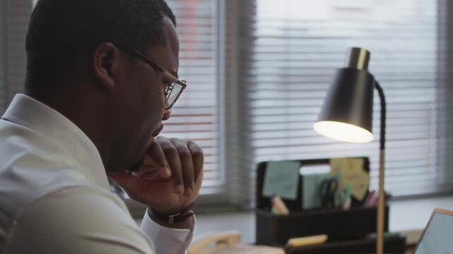 Handheld shot of African American male focused school principal working on wireless laptop while sitting at desk in office
