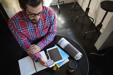 Creative man, phone and cafe with coffee above for remote work, planning or journalism. Top view, male person or freelance journalist with mobile smartphone or book for story or article in restaurant