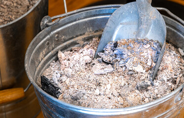 Close up of fireplace ash in a metal bucket with a scoop © Firnthirith