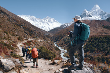 Female hiker watches group of backpackers on trail walking along river with Ama Dablam mountain in Himalayas, Nepal.
