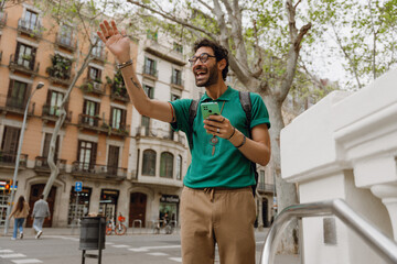 Man waving and laughing while standing and holding phone