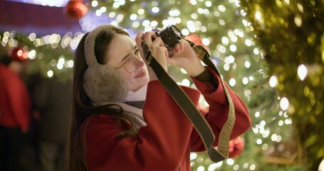 A young beautiful girl in a red coat stands near a Christmas tree with garlands and illuminations...