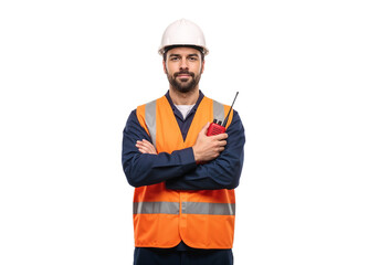 Worker in safety vest holds radio and stands with arms crossed at construction site