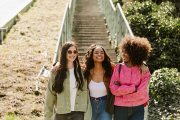 A group of three female friends laugh as they walk and one of them hugs the others