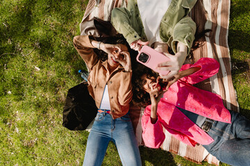A group of three female friends pose in front of a phone held by one of them while they gesturing and lie on a blanket with their heads next to each other