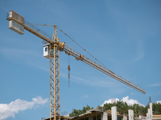 A construction crane towers next to a monolithic-frame building being built against a clear blue sky