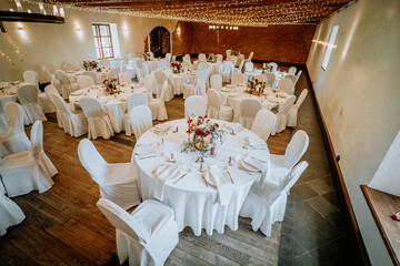 Elegant banquet hall set for a celebration with round tables adorned in white tablecloths, floral centerpieces, and soft lighting creating a warm, inviting atmosphere for gatherings