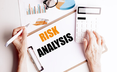 Risk analysis text on clipboard with hands using calculator and financial charts on desk