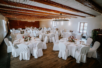 Elegant banquet hall setup with round tables adorned in white tablecloths, floral centerpieces, and twinkling fairy lights creating a romantic atmosphere for special events