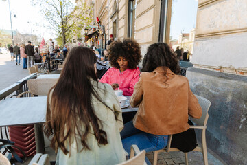 A woman stirs a drink with a spoon and sits at a table next to two female friends