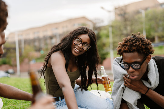 Woman smiling and holding a bottle while listening and sitting near a group of three friends - Powered by Adobe