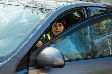 Mature woman at steering wheel of parked car with open driver door, checking surroundings before maneuvering
