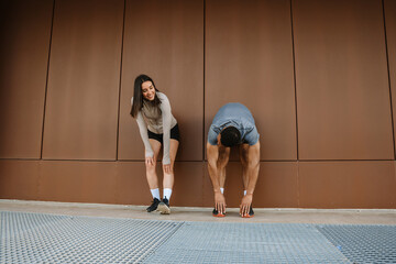 Female athlete laughing and talking to male athlete reaching for his feet while they stand and lean on a wall