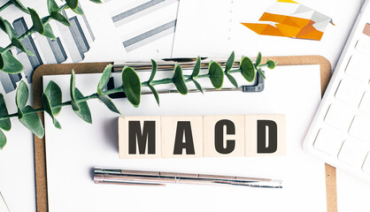 MACD abbreviation on wooden blocks with clipboard, pen, calculator and business charts in background