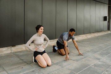 Naklejka premium A female athlete keeps her hands on her waist while a male athlete rests his hands on the ground while they kneel next to each other