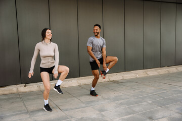 Female and male athletes smiling and reaching for their legs which they lift while he looks at her