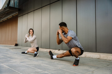 Male and female athletes squatting and stretching their legs while she smiles